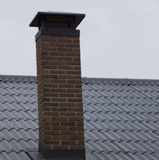 large brick chimney on the brown tiled roof of a private house against the sky